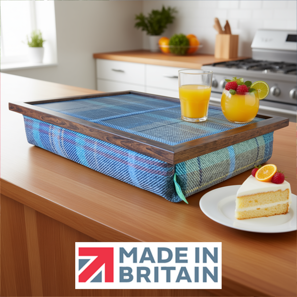 The Bedlington Tweed lap tray with wooden frame and a cushioned base, shown on a kitchen island with orange juice and cake, alongside the Made in Britain logo.