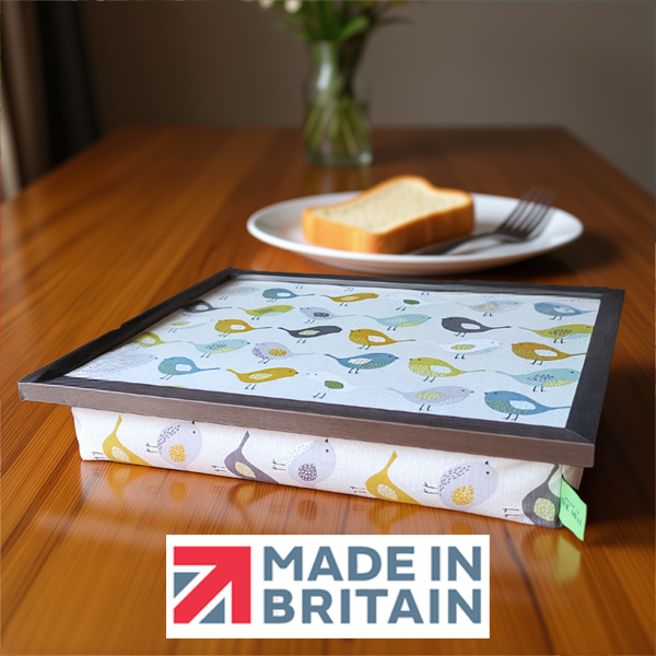A colourful bird-pattern lap tray with cushioned base, alongside the Made in Britain logo displayed on a wooden table.