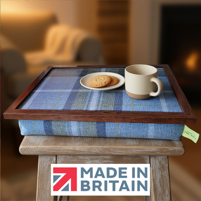 The Blue Westie Tweed lap tray with biscuits and a mug on it, alongside the Made in Britain logo, all set in a cosy living room setting.