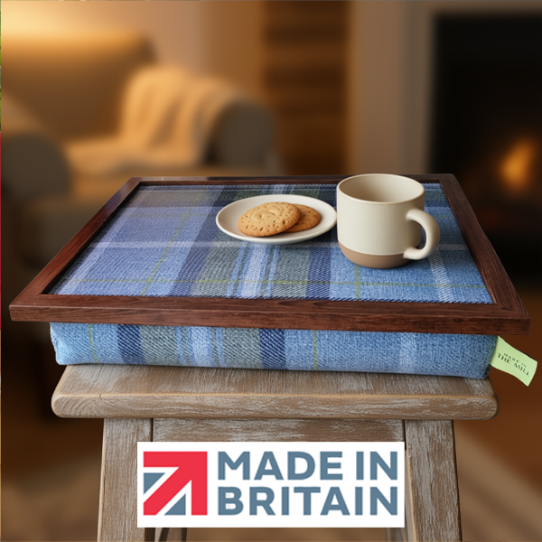 The Blue Westie Tweed lap tray with biscuits and a mug on it, alongside the Made in Britain logo, all set in a cosy living room setting.