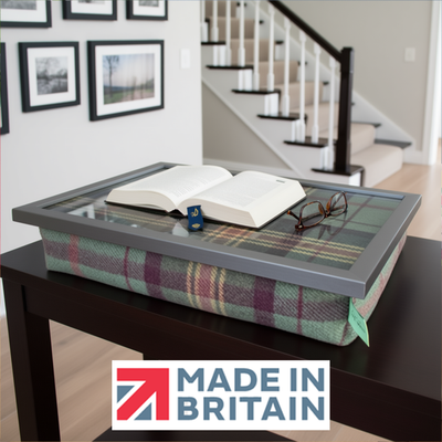 The Brittany lap tray with an open book and glasses on it, alongside the Made in Britain logo, all set in a modern day living room 