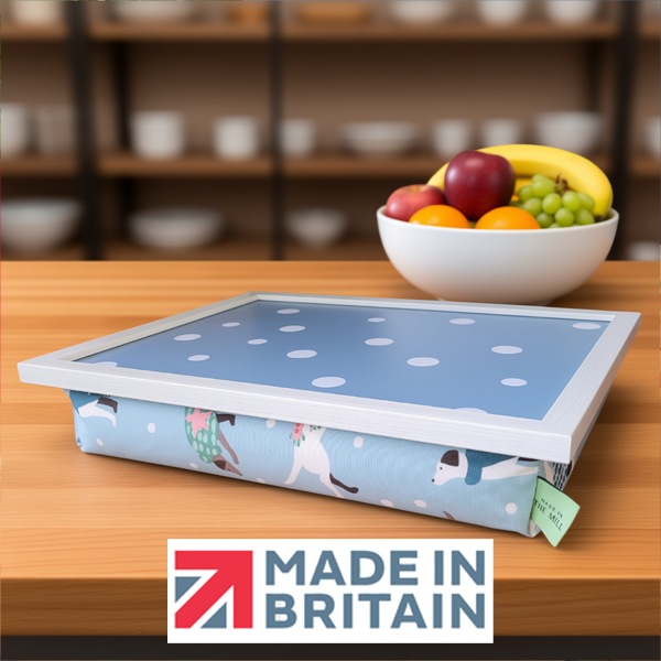 The Dapper Dogs lap tray with cushioned base, alongside the Made in Britain logo, displayed on a wooden kitchen counter beside a bowl of fruit.