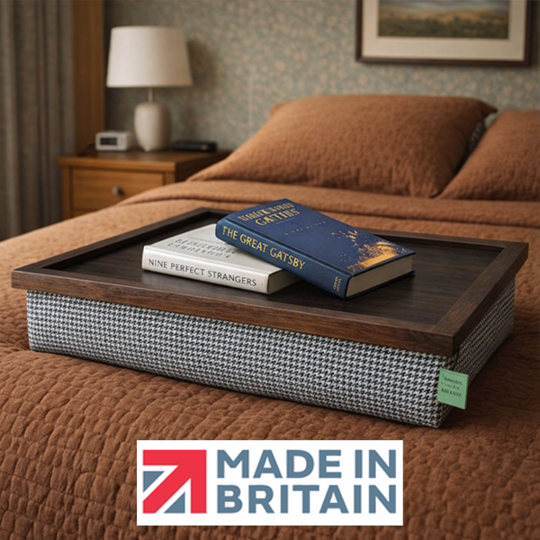 The Dogtooth lap tray with wooden frame and cushioned base on a bed, styled with two reading books, alongsidethe Made in Britain logo.