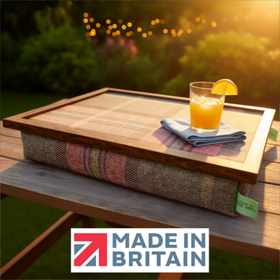 The Harrier Wweed lap tray with wooden frame and a cushioned base, displayed outdoors at sunset with a drink, alongside the Made in Britain logo.
