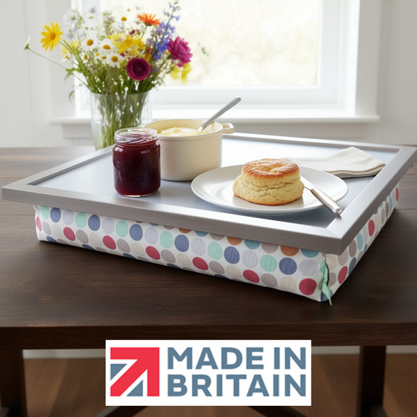The Polka Dot lap tray with silver frame and cushioned base on a dark wooden table, styled with a plate with a scone on it, a pot of jam, a knife and a pot of butter, alongside the Made in Britain logo.