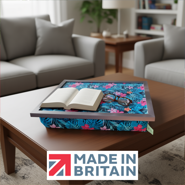 The Tropical Palm lap tray with a vibrant blue and pink design, shown in a modern living room with an open book, reading glasses, alongside the Made in Britain logo.