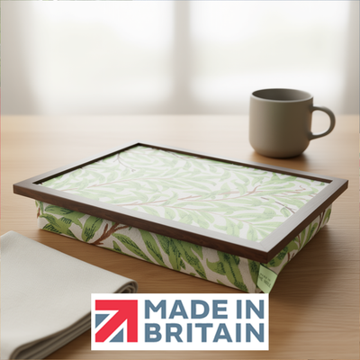 The William Morris Sage Willow lap tray with green leafy design and a wooden frame, displayed on a wooden table, alongside the Made in Britain logo.
